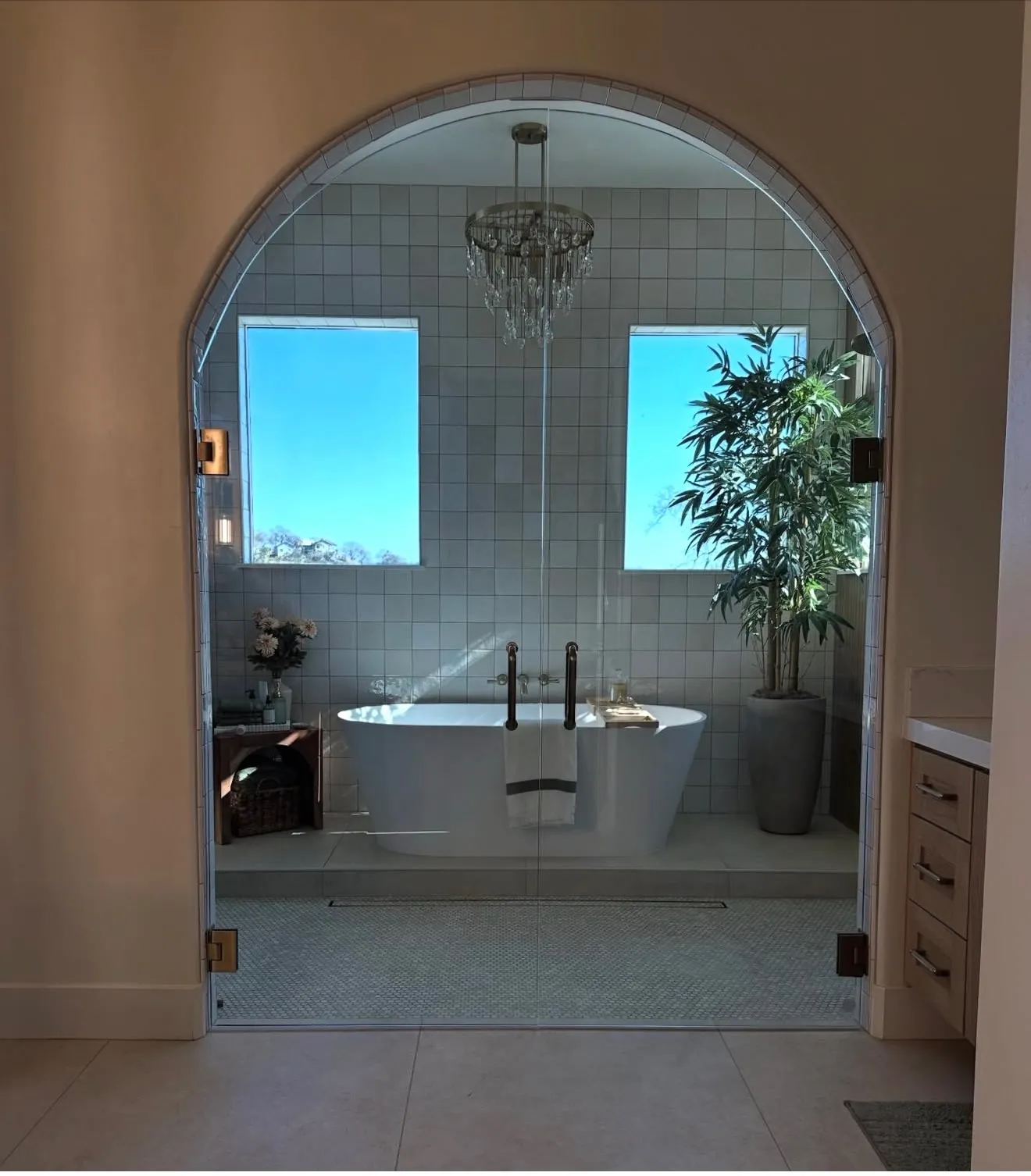 Arched glass door opening to a bathroom with a freestanding soaking tub and crystal chandelier