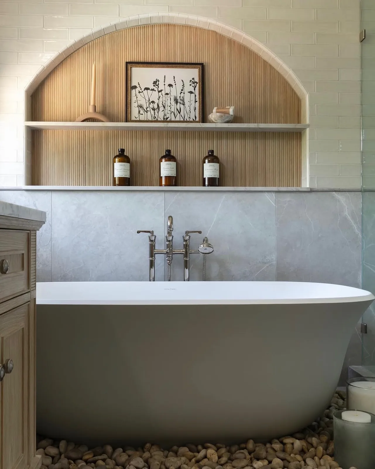 Freestanding soaking tub set beneath a fluted arched niche with a marble surround
