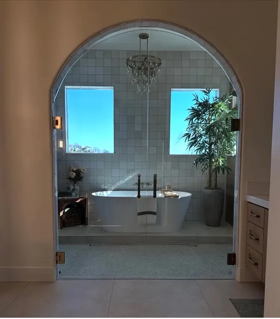 Arched glass door opening to a primary bath with a freestanding soaking tub and crystal chandelier