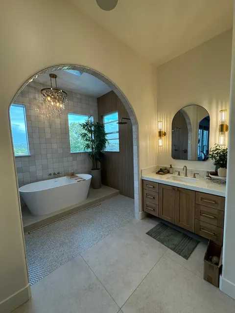 Primary bathroom with an arched tiled tub alcove, walnut double vanity and vaulted ceiling