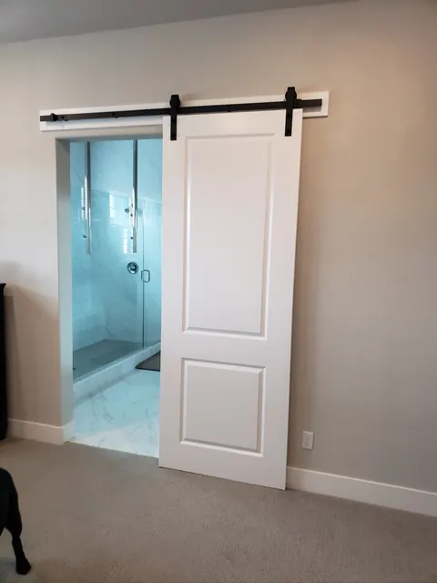 Sliding barn door opening to a primary bathroom with a frameless glass shower