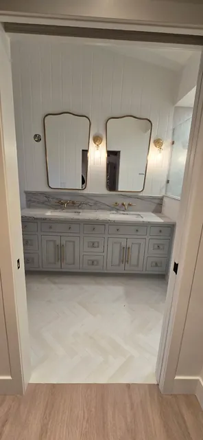 Primary bathroom double vanity with arched mirrors, brass sconces and herringbone wood flooring