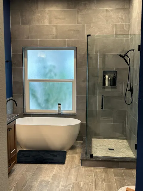 Bathroom with a freestanding soaking tub, navy walls and a frameless glass shower