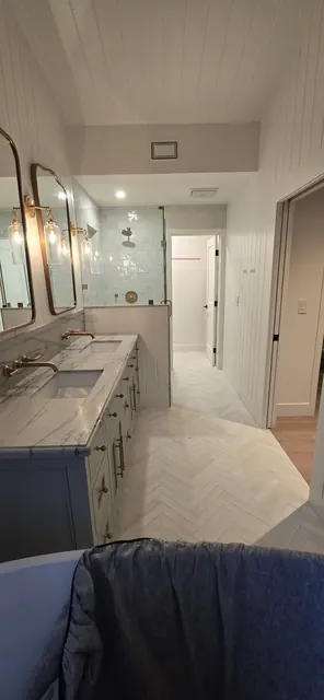 Primary bathroom with a marble double vanity, navy cabinetry and herringbone tile flooring