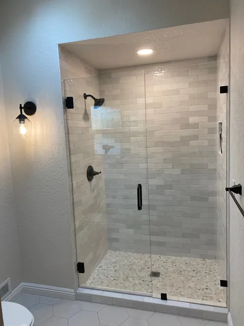 Frameless glass shower with marble tile walls and a pebble tile shower floor