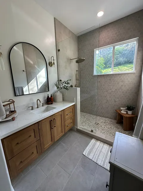 Bathroom with a white oak double vanity, arched mirror and gray tile walk-in shower