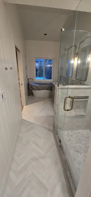 Primary bathroom remodel with a frameless glass walk-in shower, herringbone tile floor and freestanding tub beyond