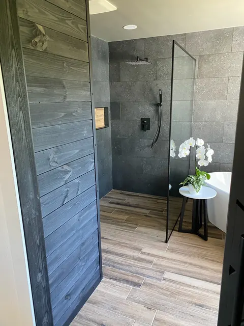 Weathered wood barn door opening to a curbless walk-in shower and freestanding tub