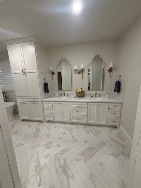Primary bathroom with a white double vanity and marble herringbone tile floor