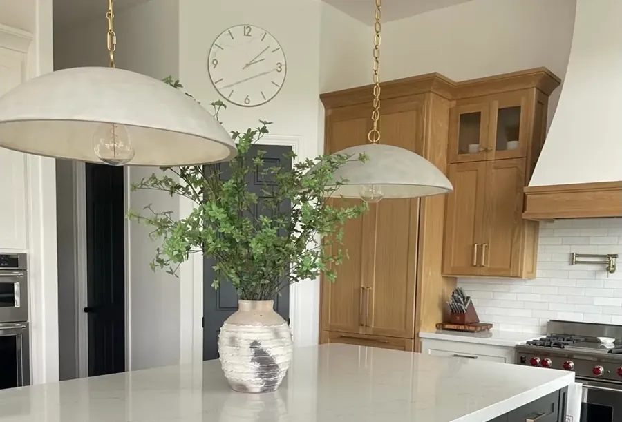 The same kitchen after remodel: white oak cabinetry, quartz counters, a custom hood and dome pendants