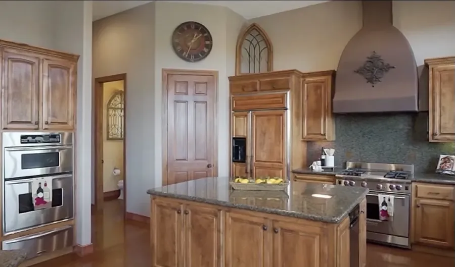 Kitchen before remodel: maple cabinets, granite counters and a plaster range hood over dark tile flooring