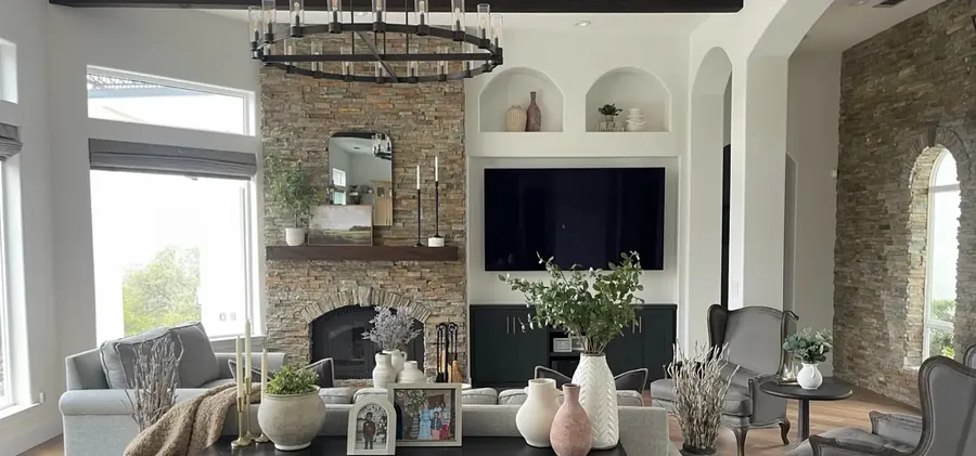 The same living room after remodel: refinished stone fireplace, dark built-ins, iron chandelier and light flooring