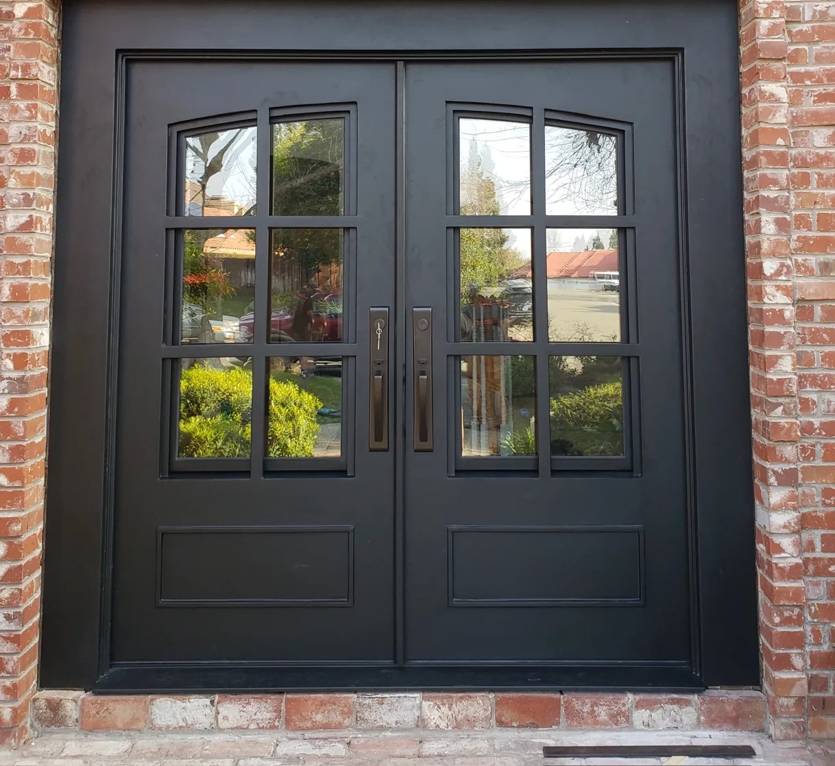 Custom black steel entry doors with divided-light glass set into a brick facade