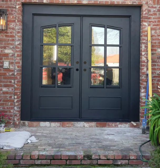 Black steel French entry doors with divided-light glass set into a brick facade