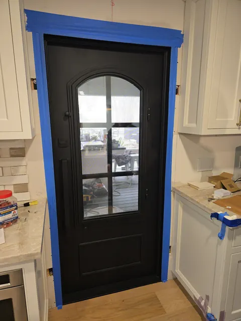 Custom black steel and glass entry door installed off a white kitchen with quartz countertops