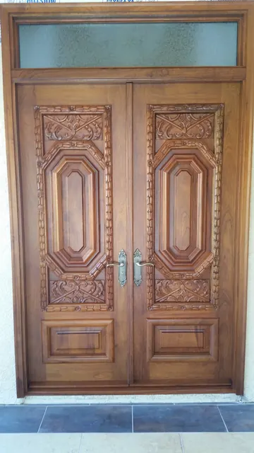 Hand-carved wood double entry doors with a transom window and stone entry landing