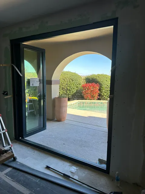 Multi-panel glass door opened to a poolside patio and arched garden wall