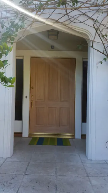 Wood front entry door beneath a covered arbor entry with tile porch flooring