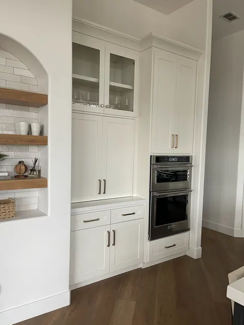 Custom butler's pantry with white cabinetry, glass-front uppers and built-in double wall ovens