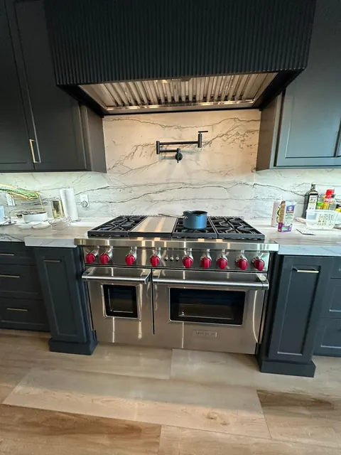 Dark green kitchen with a professional range, brass pot filler and quartzite backsplash