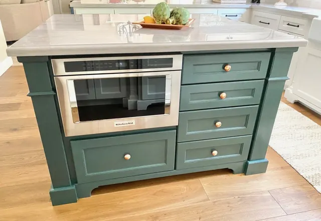 Custom green kitchen island with a built-in microwave, brass knobs and quartz countertop
