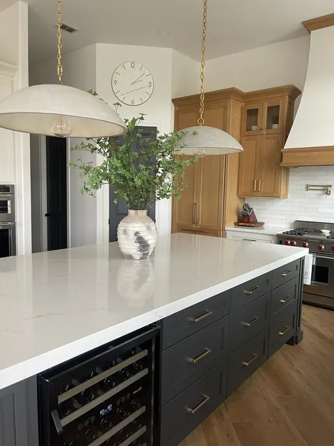 Kitchen with a navy island, brass hardware, built-in wine refrigerator and white oak range hood