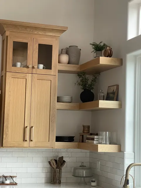 White oak pantry cabinet with glass doors and floating corner shelves above a subway tile backsplash