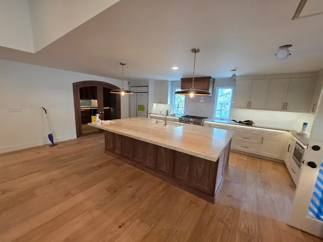 Open-concept kitchen remodel with a large walnut island, stone countertops and white cabinetry