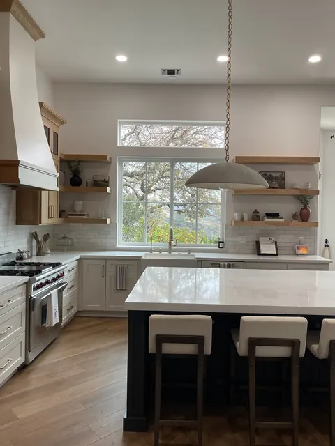 Kitchen with a custom plaster range hood, black island seating and floating oak shelves