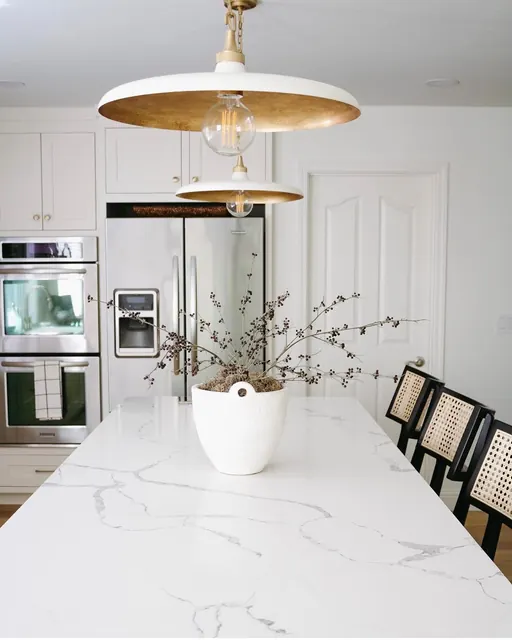 Kitchen island in veined quartz with cane counter stools and built-in double wall ovens