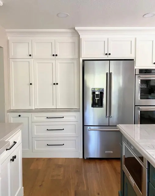 Floor-to-ceiling white kitchen cabinetry framing a counter-depth refrigerator and built-in ovens