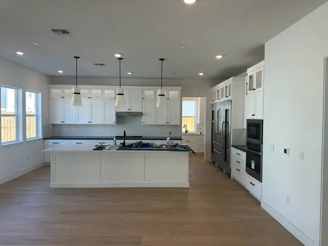 Bright white kitchen remodel with a long center island, pendant lighting and stainless appliances
