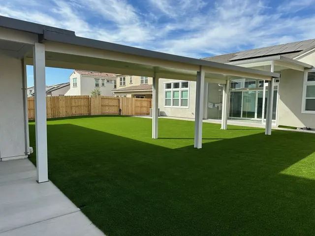Covered patio with painted posts overlooking a backyard of artificial turf