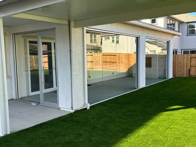 Covered patio with multi-slide glass doors opening to an artificial turf lawn
