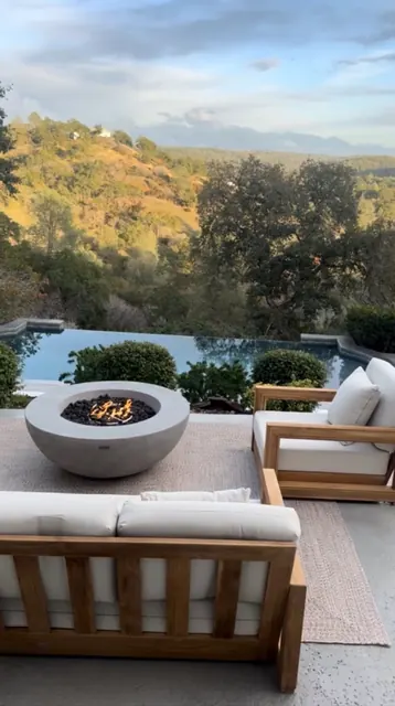 Poolside terrace with a round gas fire pit, teak lounge seating and a hillside view