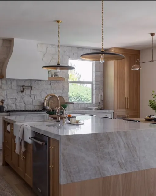 Renovated kitchen with a marble island, stacked stone backsplash, oak cabinetry and brass fixtures