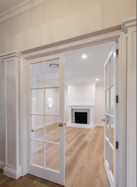 Interior French doors opening from a hallway into a remodeled living room with a marble fireplace