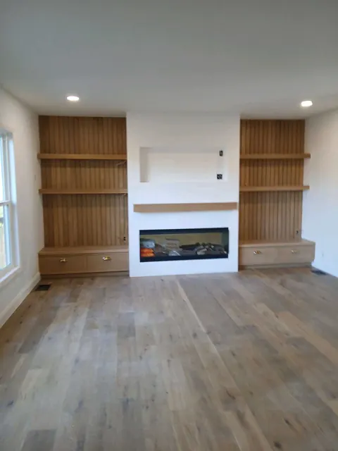 Living room with custom built-in shelving flanking a linear gas fireplace and new plank flooring